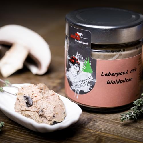 Mangalitza Leberpaté in einer kleinen Schale mit einem Champinion und dem Glaß im Hintergrund.